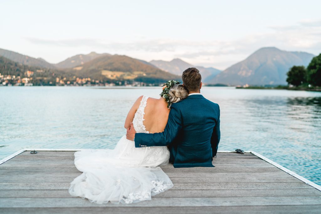 Glückliches Brautpaar umarmt sich auf einem Holzsteg am See | Strauß & Fliege