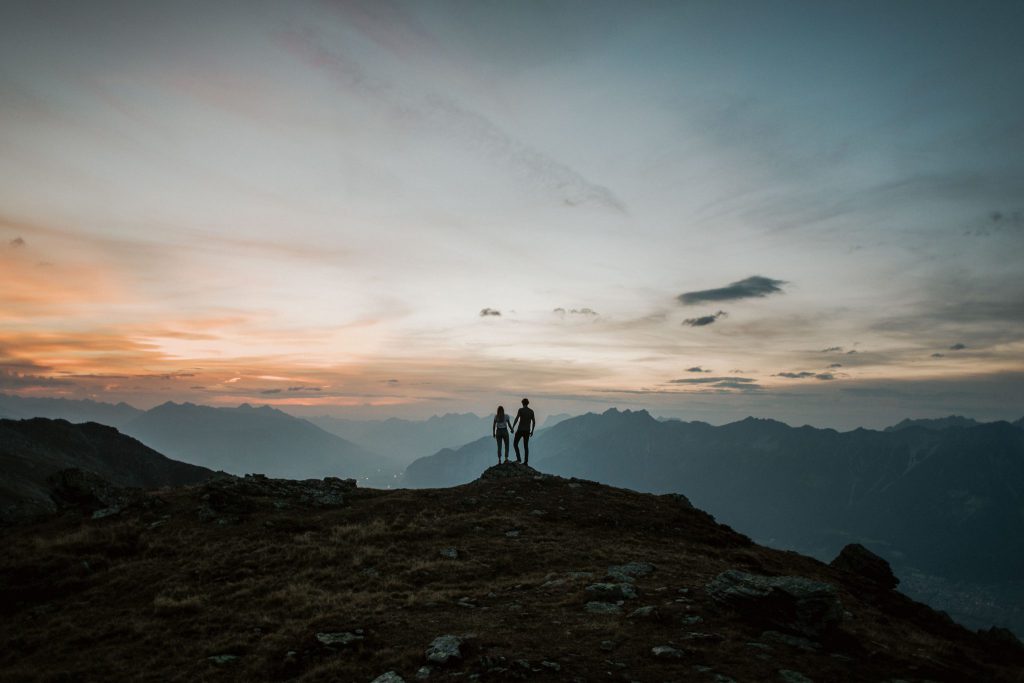 Paar auf Bergspitze vor Panorama im Sonnenuntergang