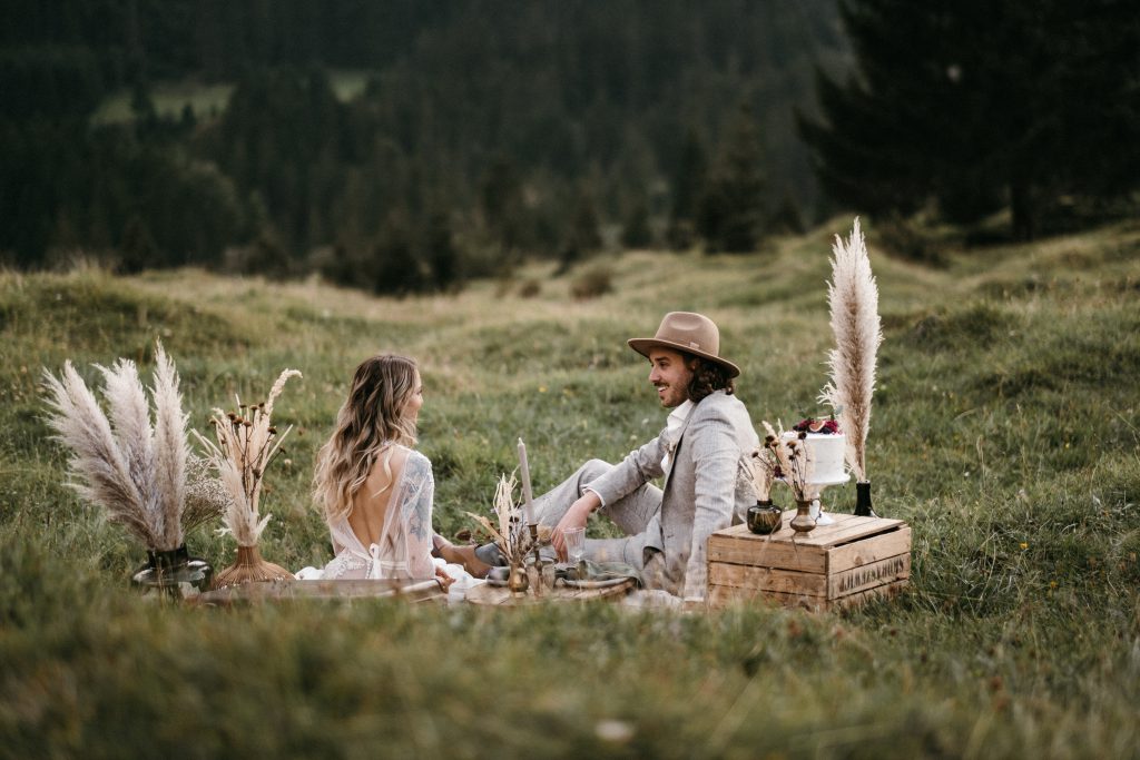 Elopement Brautpaar unter Blumenbogen beim Picknick auf einer Wiese