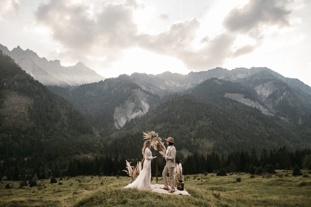 Elopement Brautpaar unter Blumenbogen auf einer Wiese mit Bergpanorama