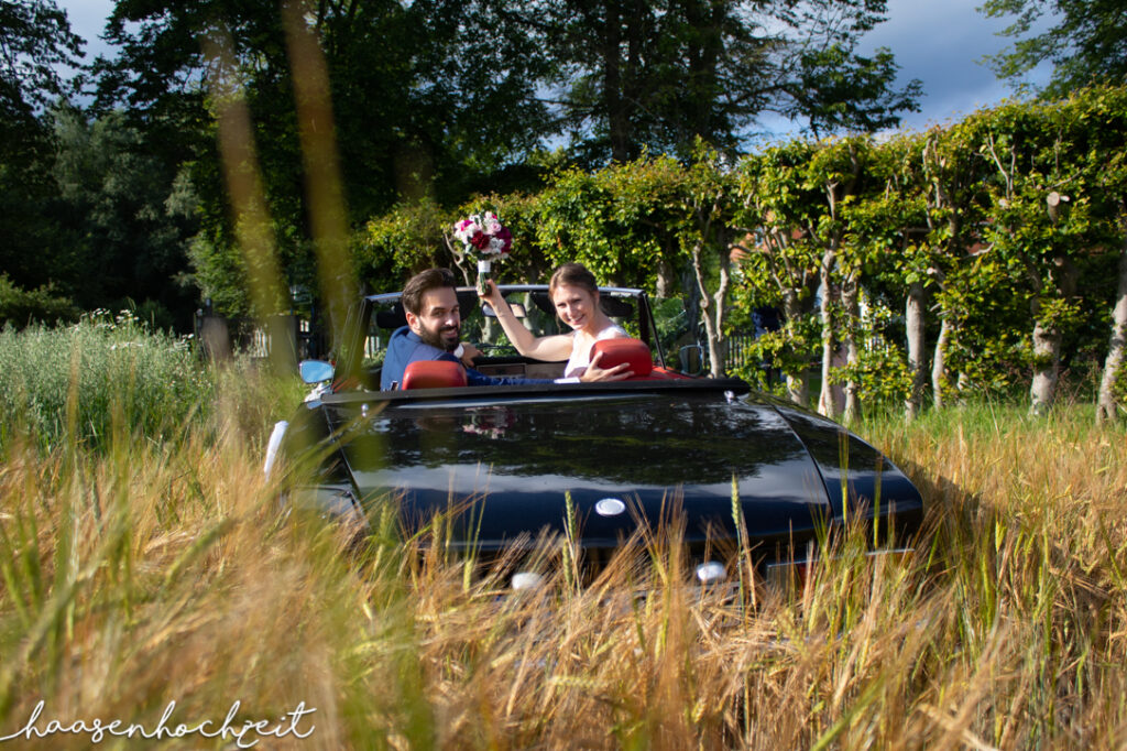 Brautpaar im Hochzeitswagen in einer Sommerwiese | Strauß & Fliege