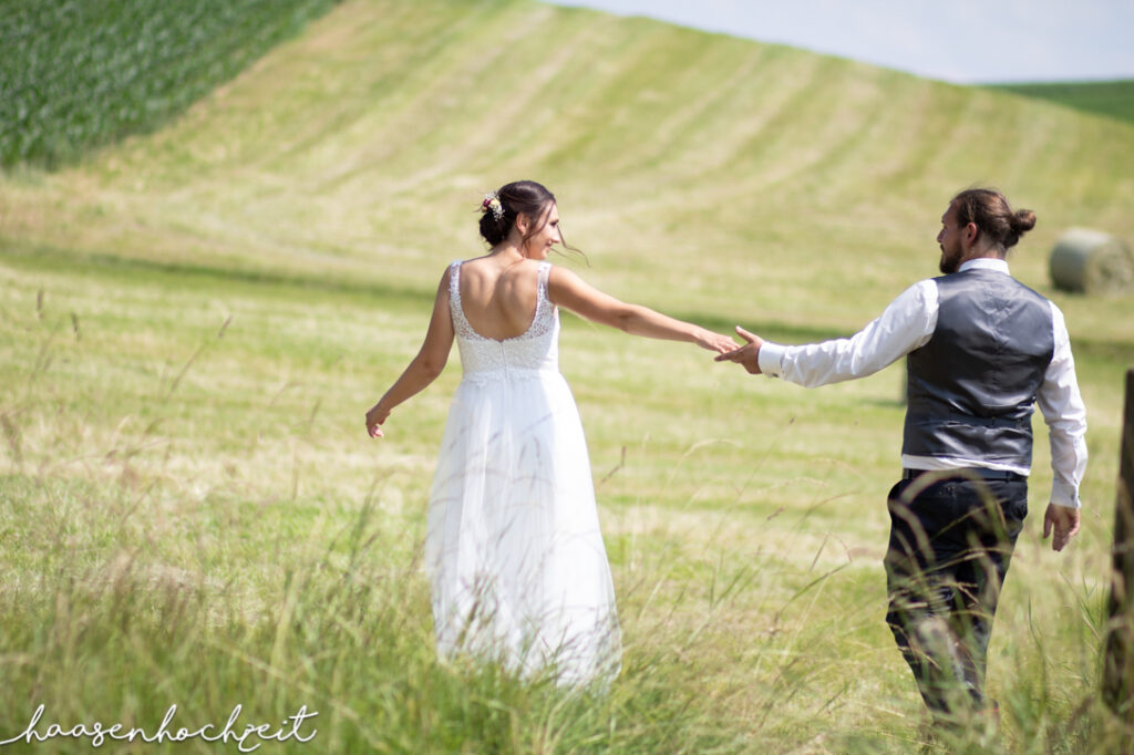 Brautpaar flaniert über Sommerwiese | Strauß & Fliege