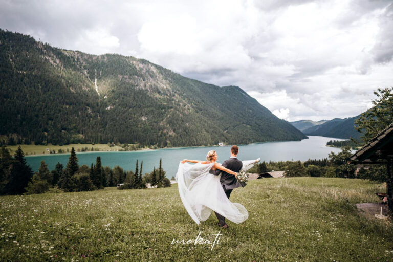 Brautpaar tanzt auf einer Wiese an einem Bergsee | Strauß & Fliege