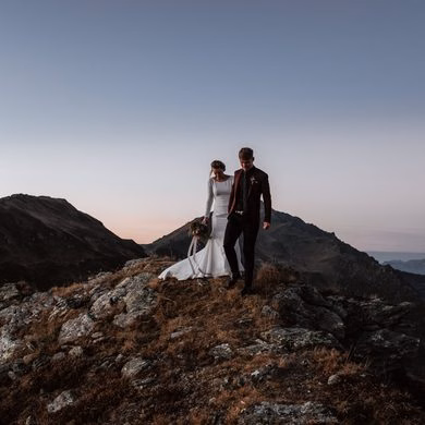 Ein Hochzeitspaar geht gemeinsam über einen felsigen Bergrücken.
