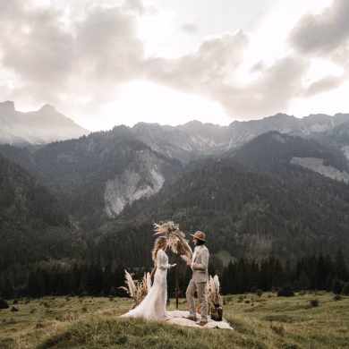 Elopement Brautpaar unter Blumenbogen auf einer Wiese mit Bergpanorama