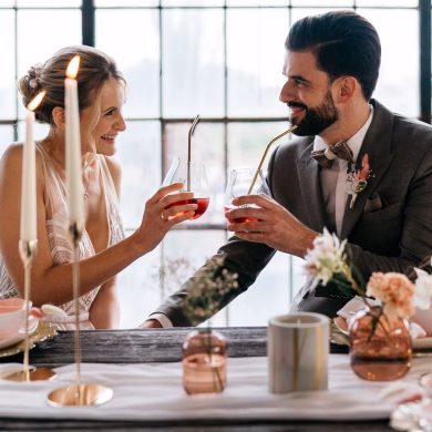 Hochzeitspaar stößt an einer gedeckten Tafel miteinander an.